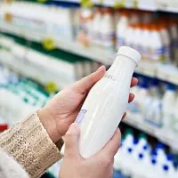 Person h&auml;lt Milchflasche im Supermarkt fest
